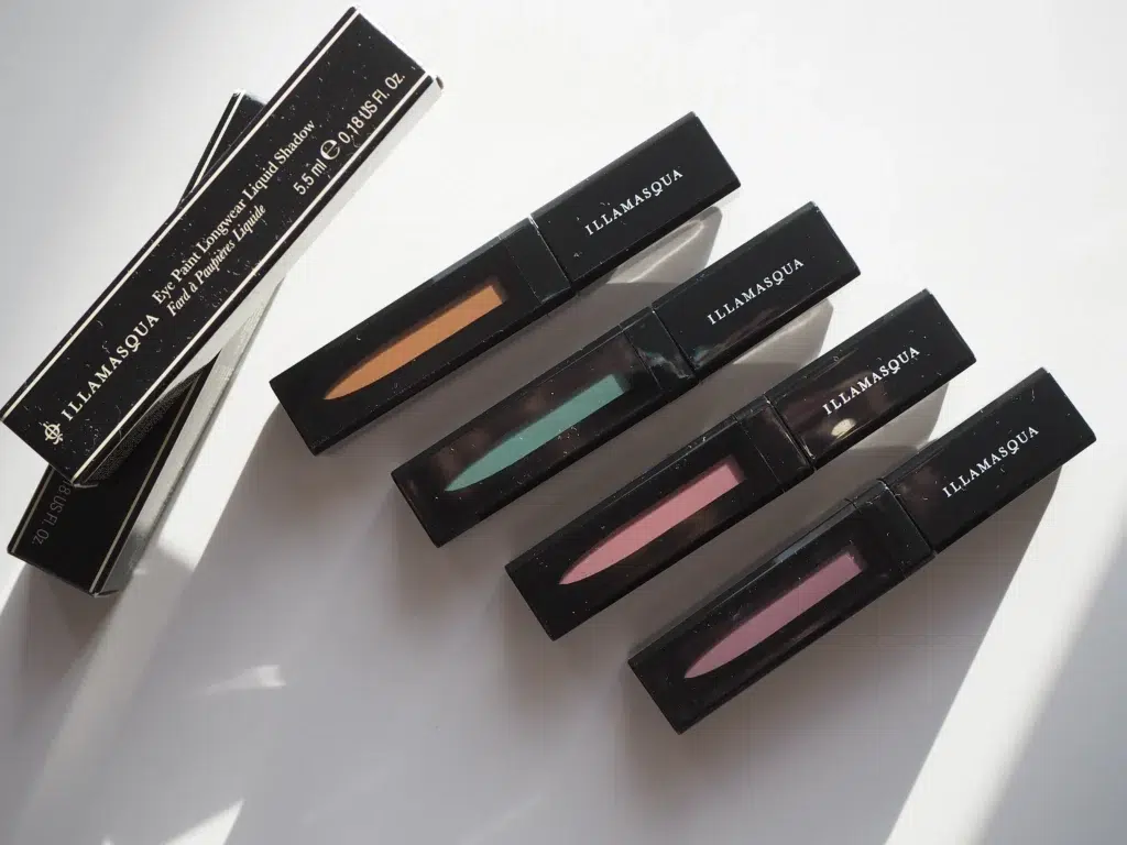 ''Illamasqua'' šķidrās acu ēnas dažādās krāsās uz balta galda.