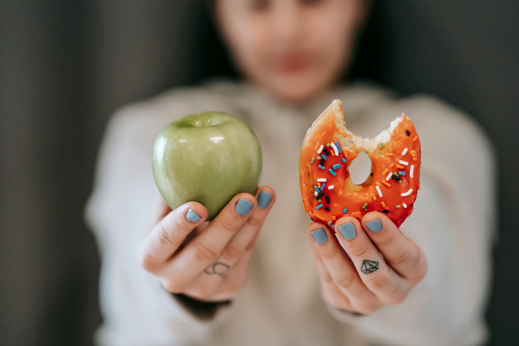 Meitene tur rokā ābolu un donutu.