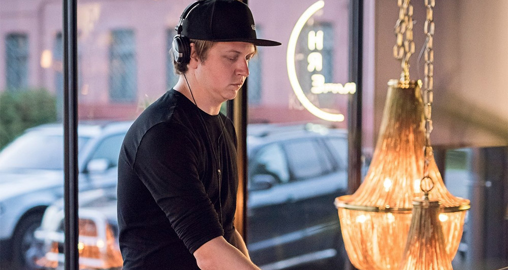 DJ Kārlis Ķilkuts ar melnu cepuri, melnu kreklu un austiņām.