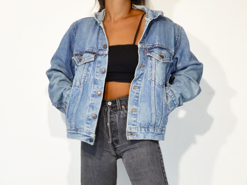 Sieviete pozē priekšā baltam fonam ar dzinsa, zilu ''Levi's'' jaku.