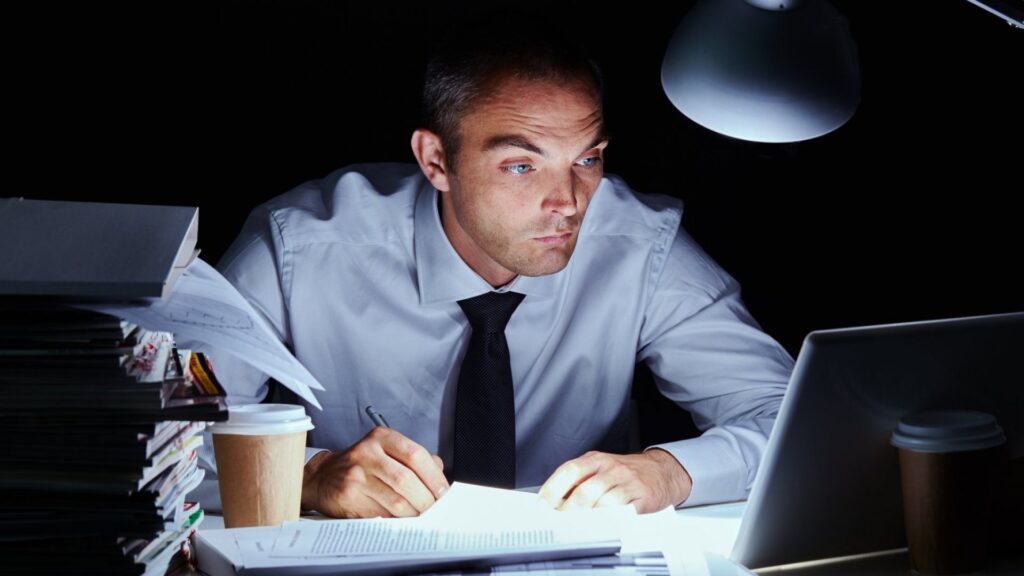Vīrietis sēž pie galda un strādā vēlā naktī.