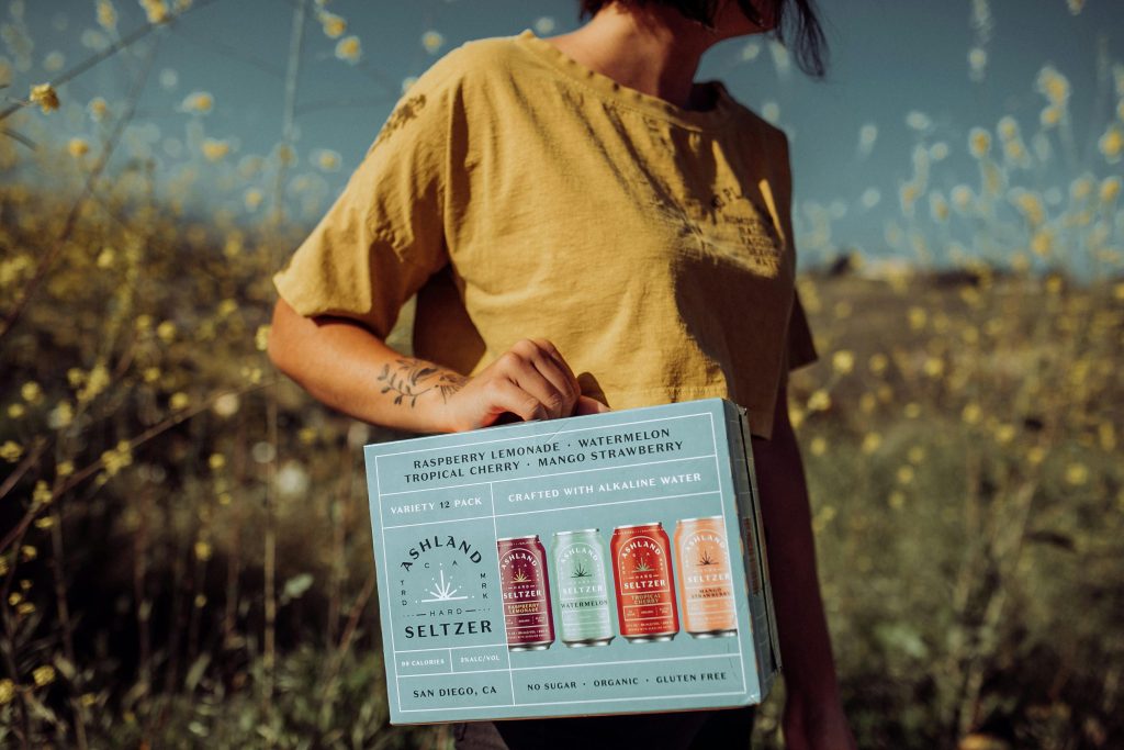 Cilvēks tur gaiši zilu kasti ar. bezglutēna alkoholiskajiem dzērieniem