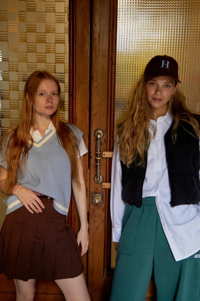 Divas meitenes preppy apģērbā stāv pie koka durvīm