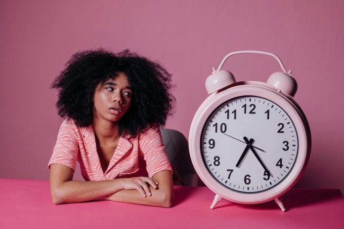 Sieviete ar afro frizūru skatās uz lielu pulksteni