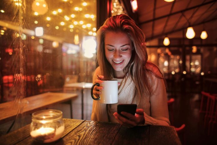 Sieviete skatās telefonā, sēžot pie galda