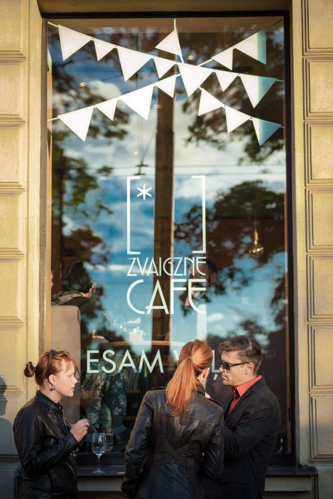 Trīs cilvēki stāv pie Zvaigzne CAFE loga