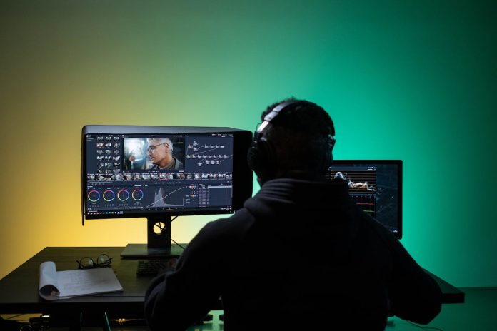 Vīrietis sēž pie datora un rediģē videoklipu