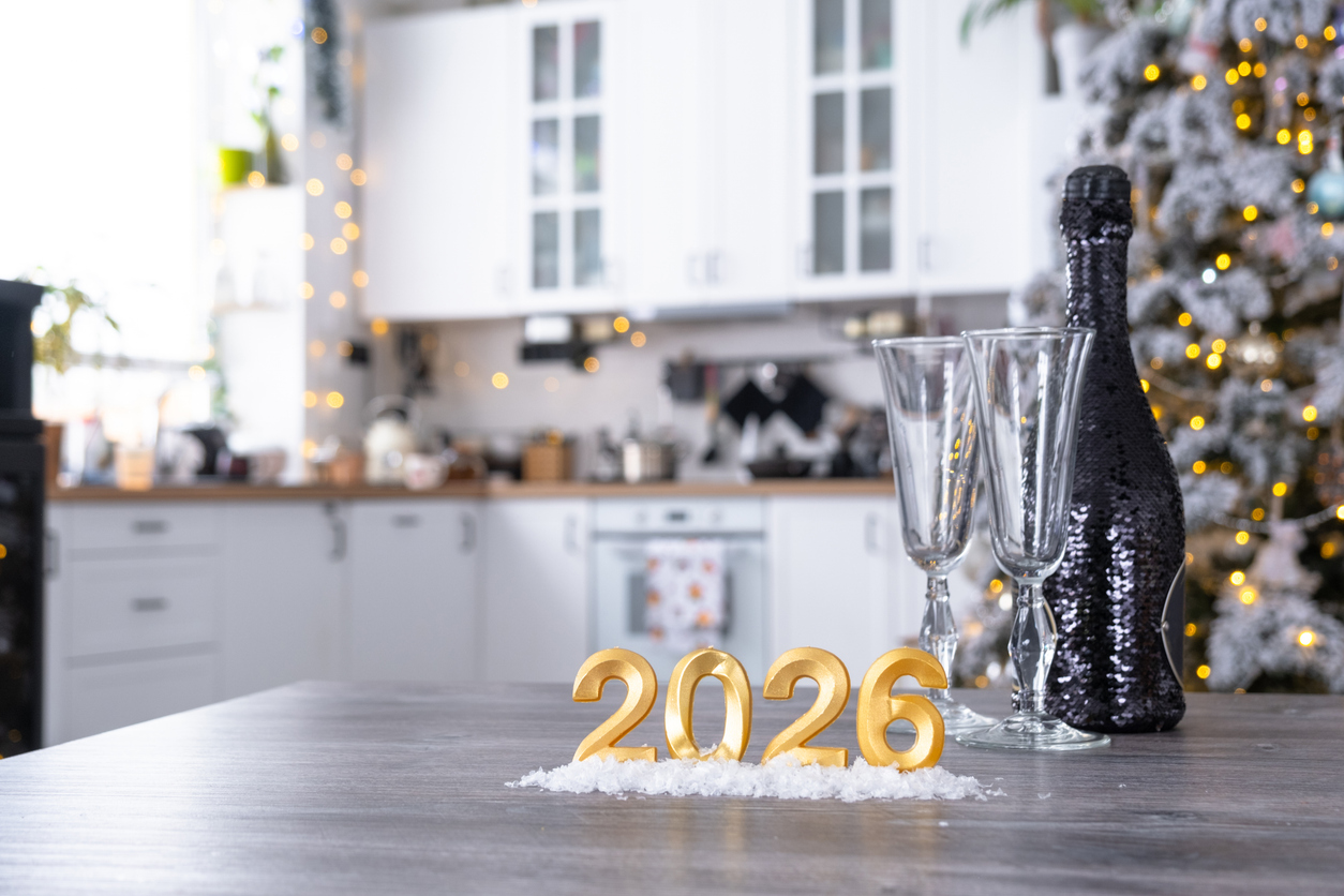 uz galda stāv zelta 2026 cipari un blakus pudele ar glāzēm