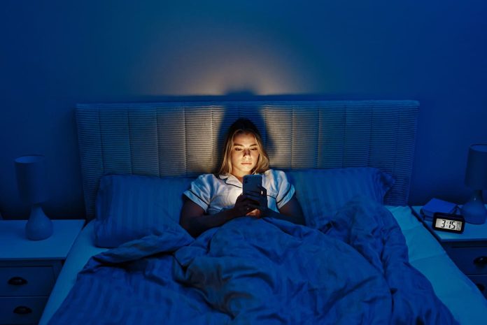 Sieviete scrolle telefonu naktī gultā